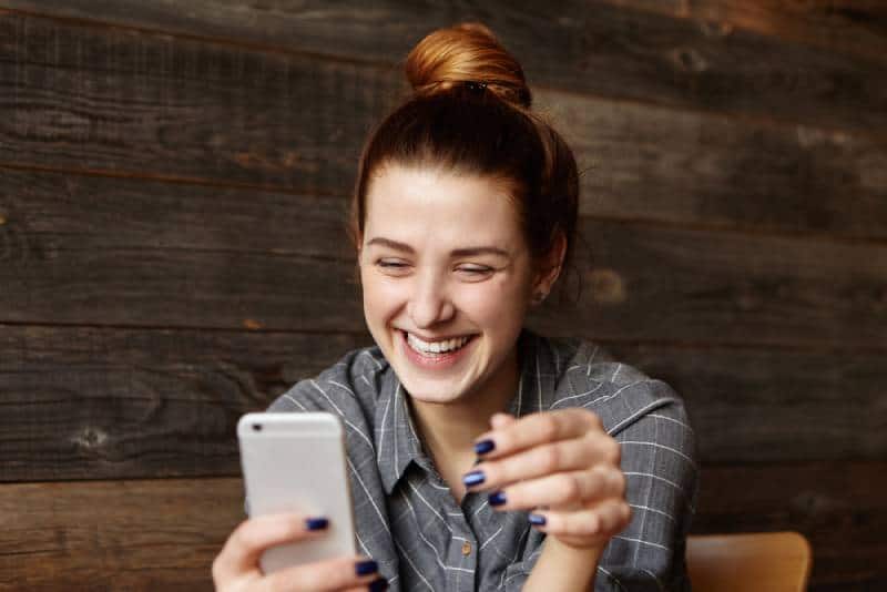 rapariga sorridente a olhar para o telemóvel num café