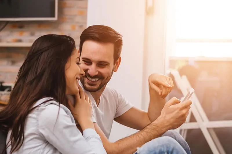 smiling man showing something on his phone to smiling woman