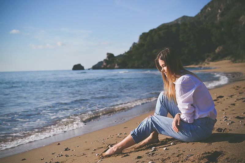 donna infelice seduta sulla spiaggia