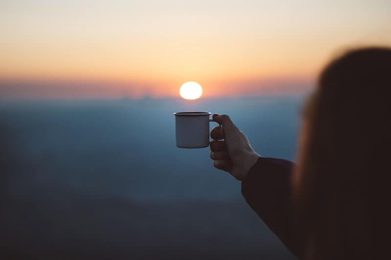 mulher a segurar uma chávena ao pôr do sol