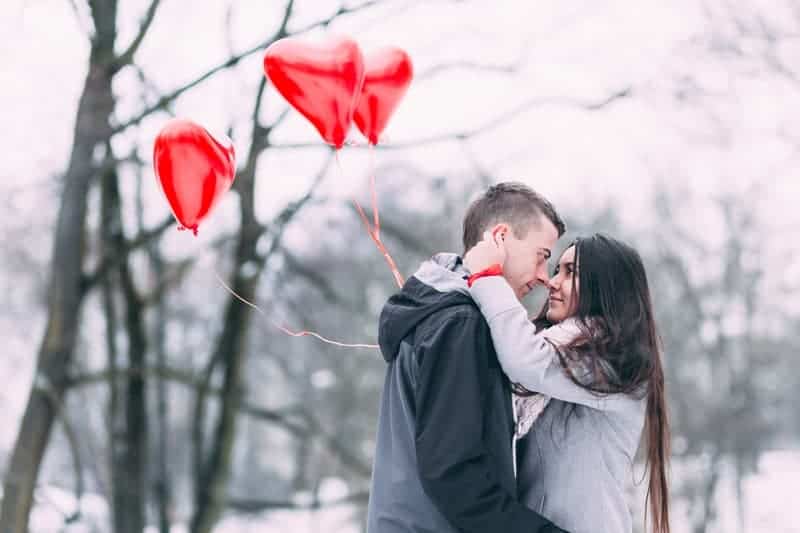woman holding heart balloon and looking at her man