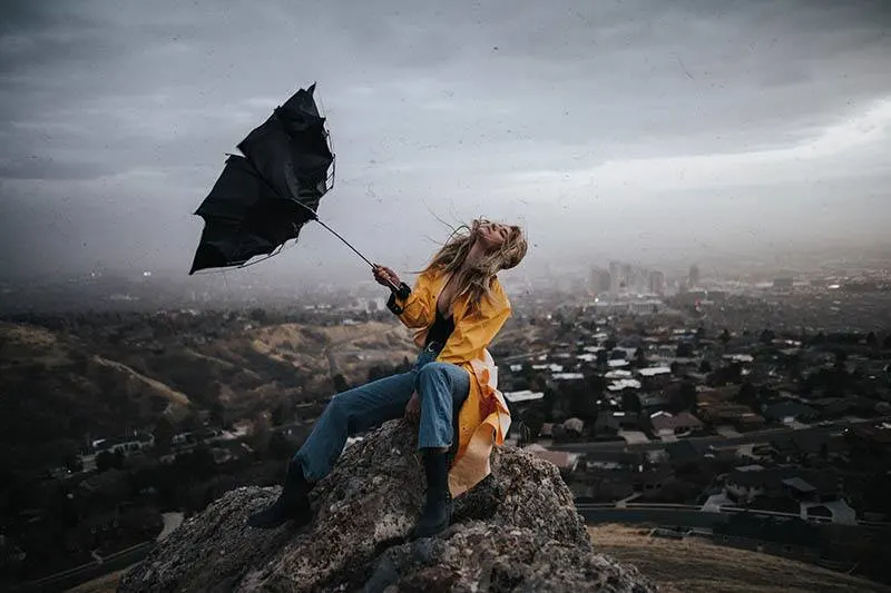 woman holding umbrella while sitting on rock outside