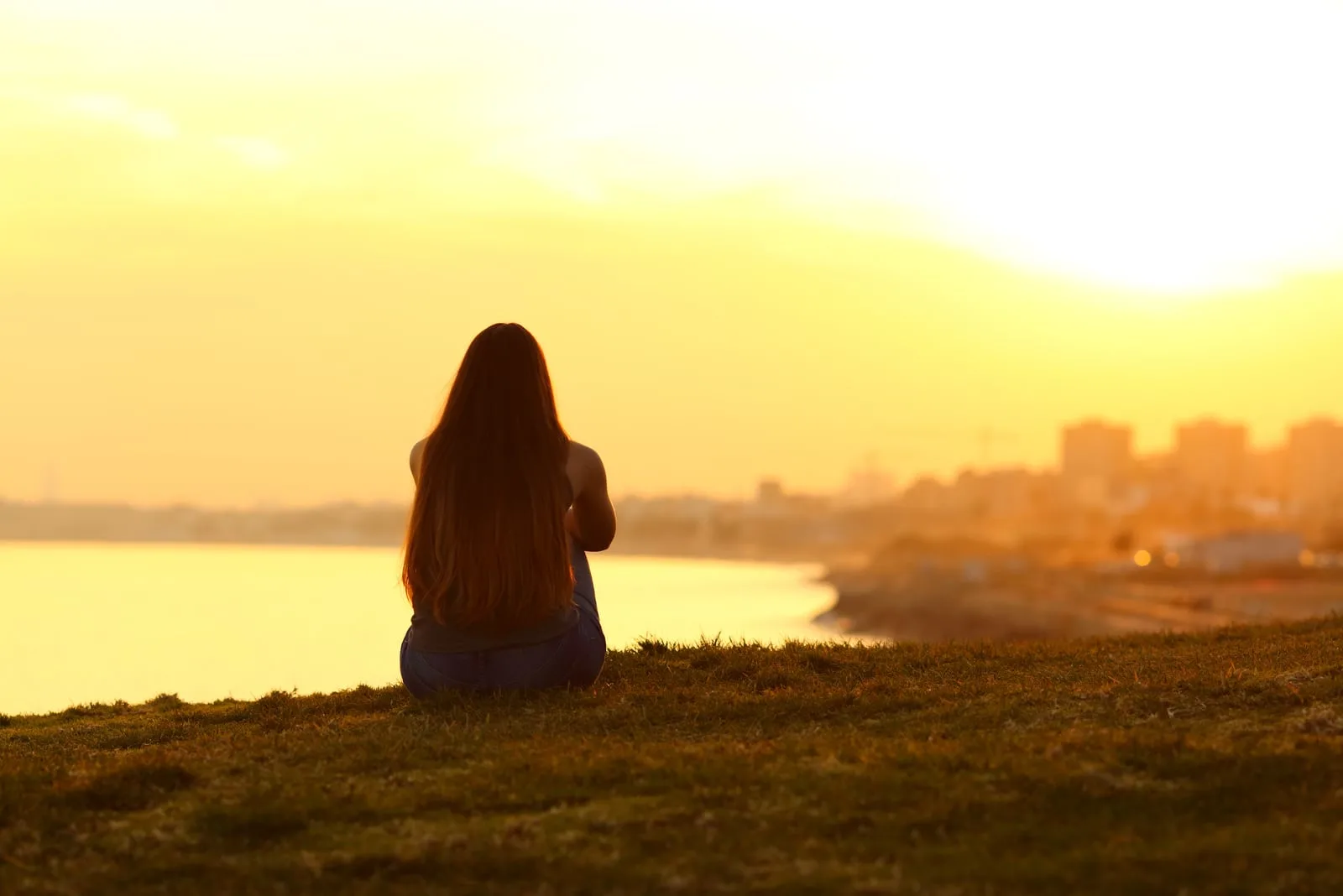  woman sitting on the grass, watching sunset 