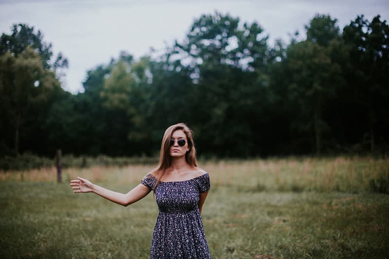 donna con occhiali da sole in piedi nel bosco