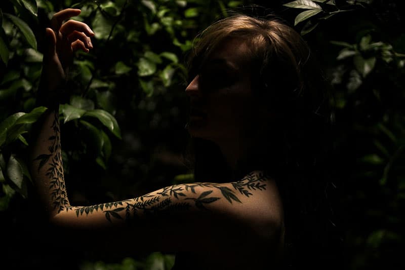donna con braccio tatuato in posa nell'oscurità