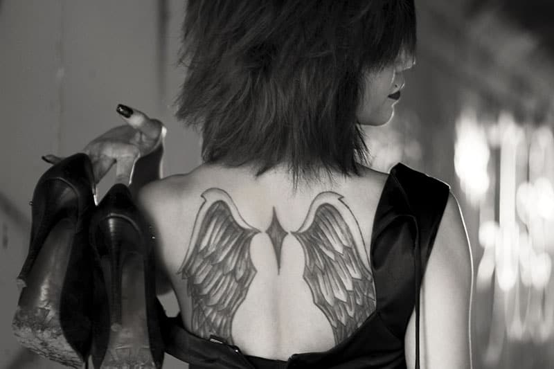woman with wings tattoo on her back holding heels