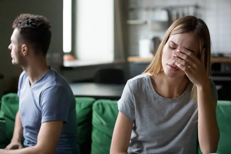 worried woman sitting on the couch with annoyed boyfriend