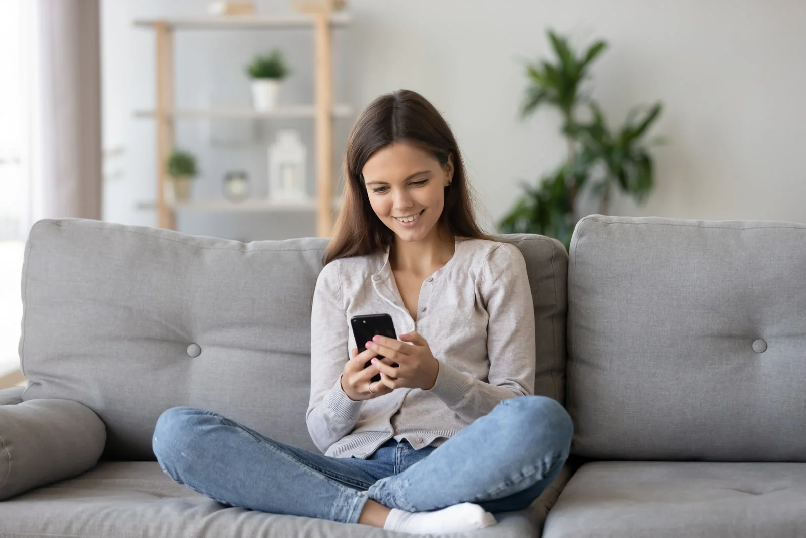 young smiling woman sitting on the couch and looking at phone