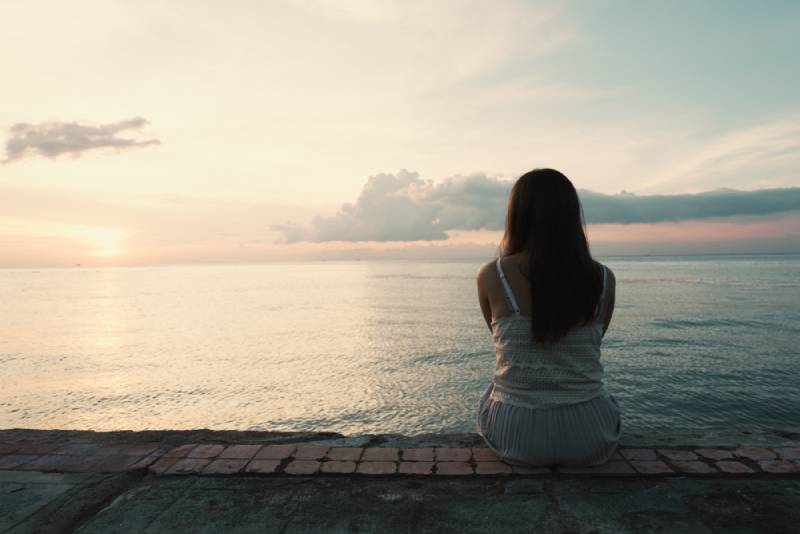 giovane donna seduta da sola sul retro, all'aperto, sulla spiaggia di un'isola tropicale
