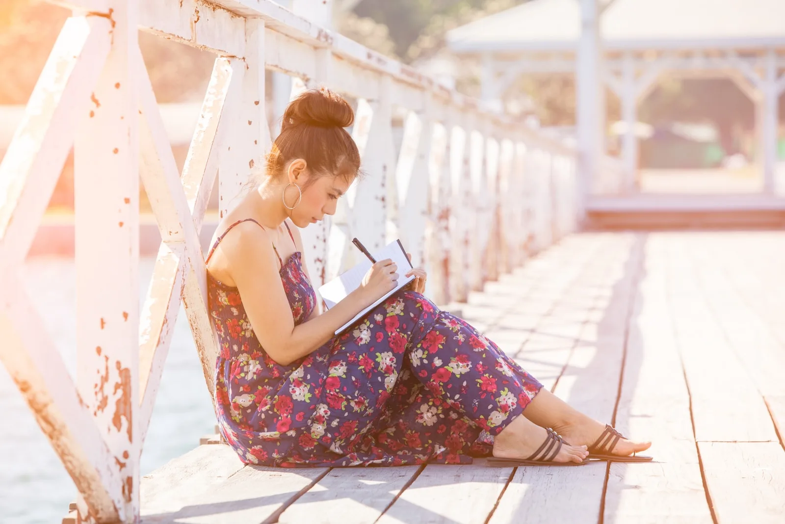 young woman sitting on the bridge and writing in the notebook