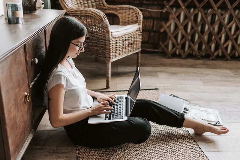 giovane donna che scrive su un computer portatile sul pavimento