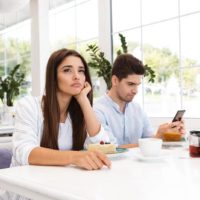 bored woman sitting while man typing on phone