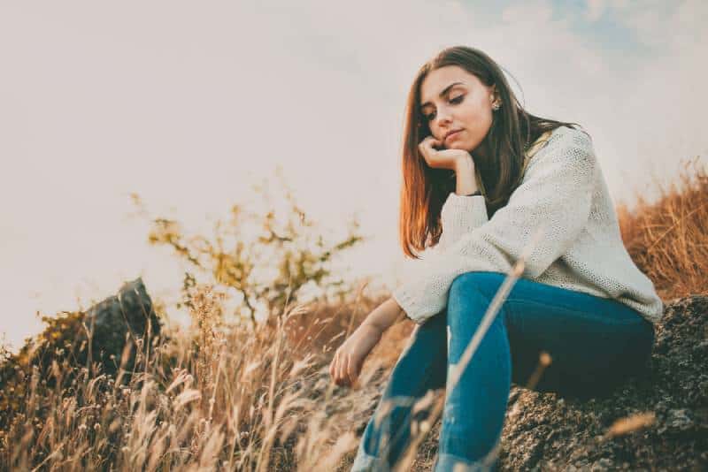 Uma jovem triste sentada sozinha numa pedra ao ar livre