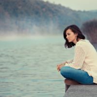 mujer pensativa sentada sola junto a un lago