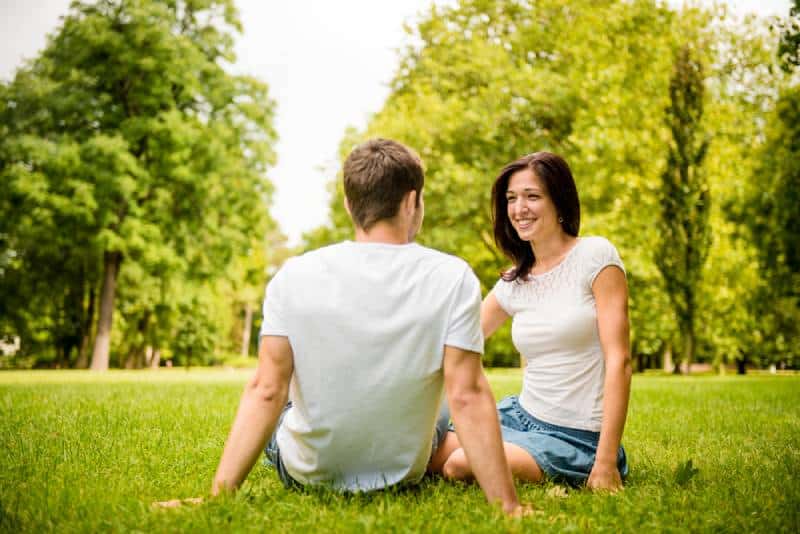 Giovane coppia felice che chiacchiera all'aperto - seduta sull'erba