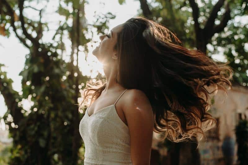 side view of cheerful woman wearing white dress in nature