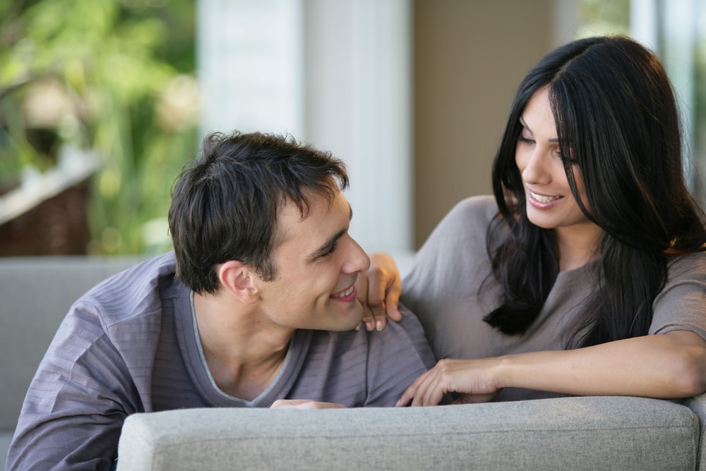 una coppia sorridente e innamorata, seduta sul divano e che si guarda l'un l'altra