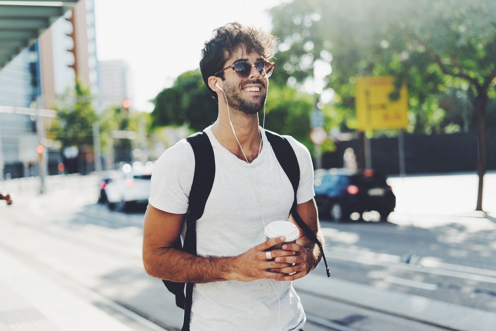 an attractive man with a backpack and sunglasses walks down the street