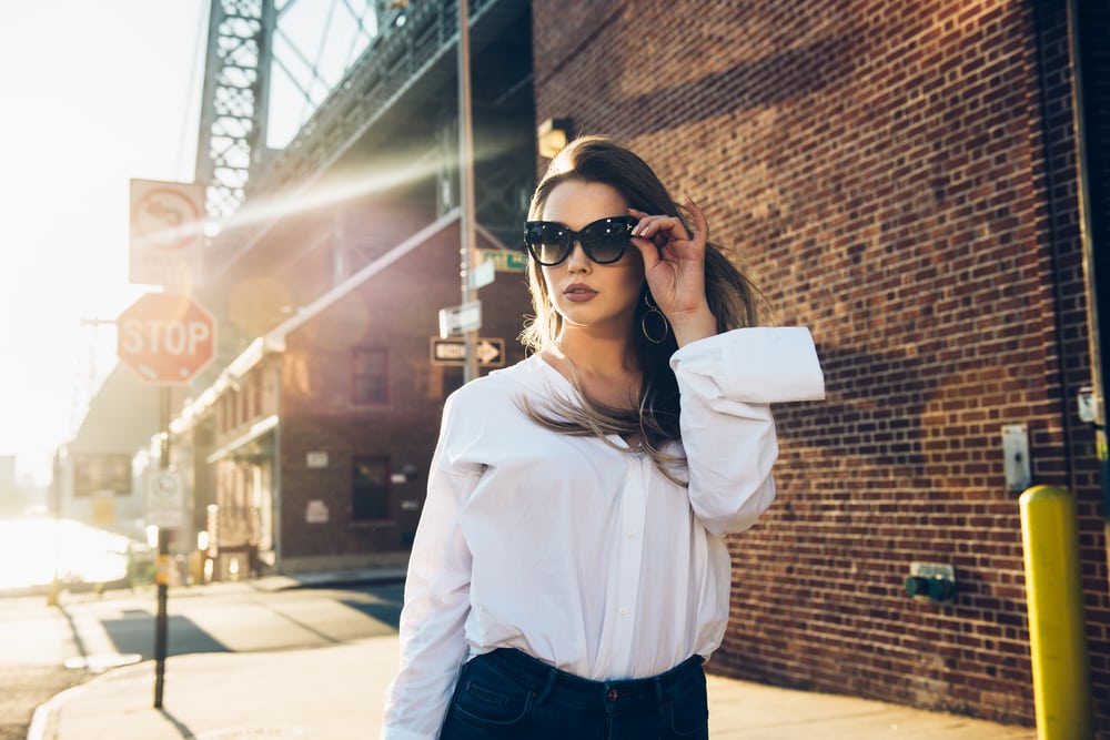 atractiva morena con gafas de sol y camisa blanca camina por la calle