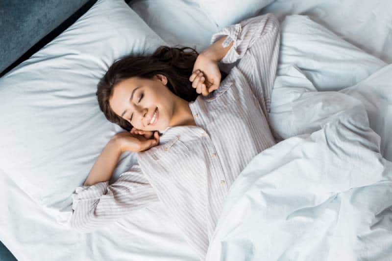 Giovane donna attraente in pigiama che si sveglia nel letto al mattino