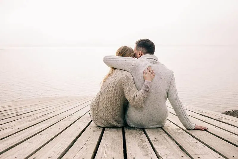back view of couple sitting on wooden dock and hugging