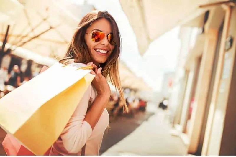beautiful smiling woman wearing sunglasses and holding shopping bag