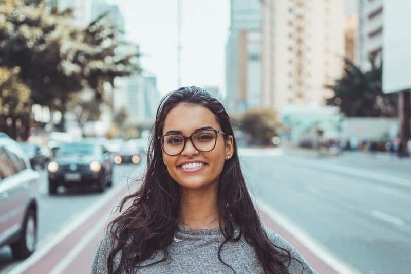 mulher sorridente, jovem e bonita, de pé na rua, com óculos