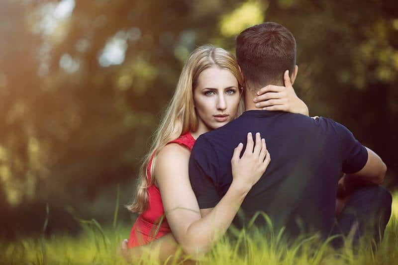 blond serious woman hugging man on the grass