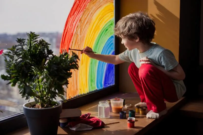 child drawing rainbow on window