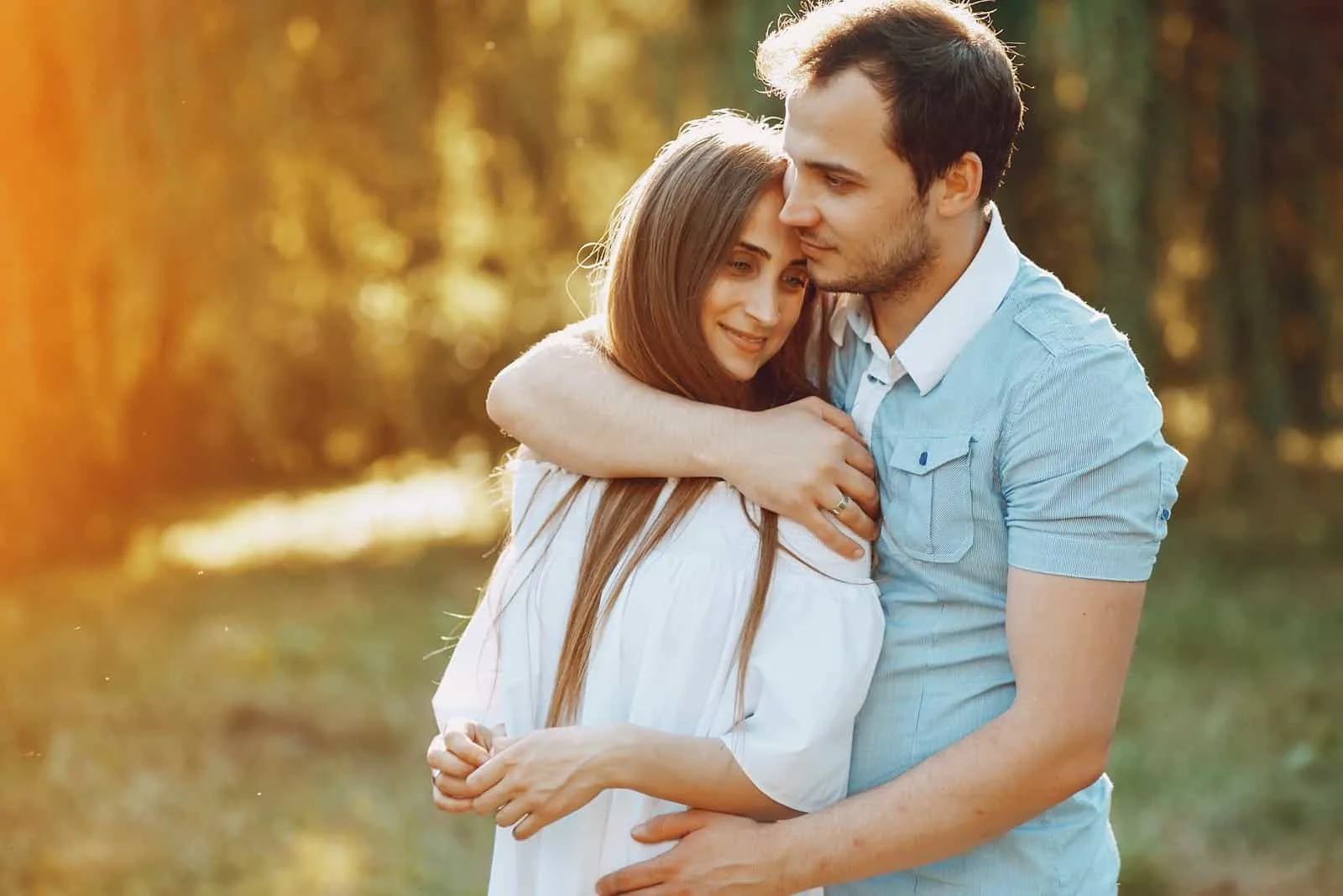 in nature a man hugs a smiling woman from behind