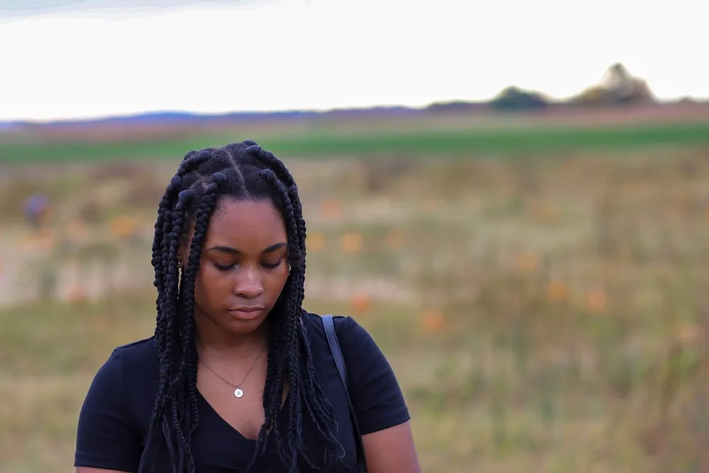 in the field stands a sad African American woman with braids