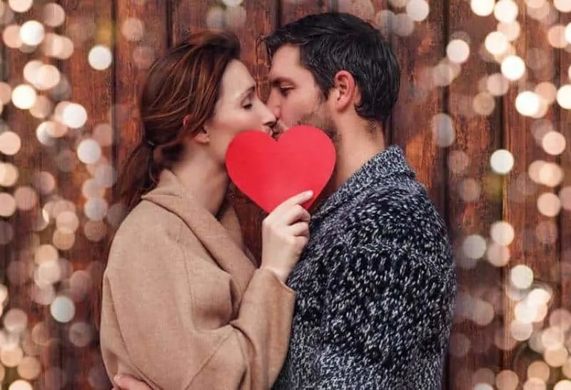 man and woman kissing while woman holding paper shape of heart