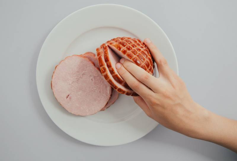 person holding sliced ham in white ceramic plate