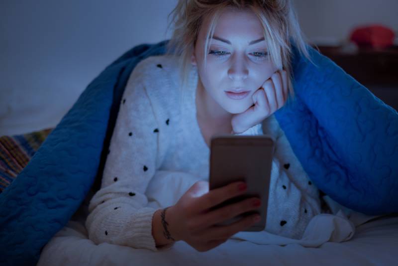 sad woman using her phone during night while lying on bed