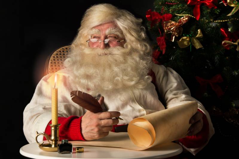 santa claus sentado en casa y escribiendo en un rollo de papel viejo