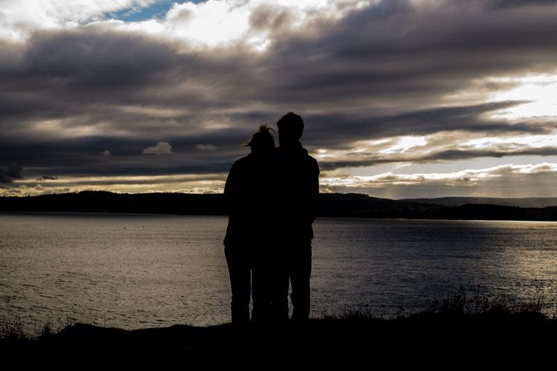 silhouette of couple hugging in front of lake