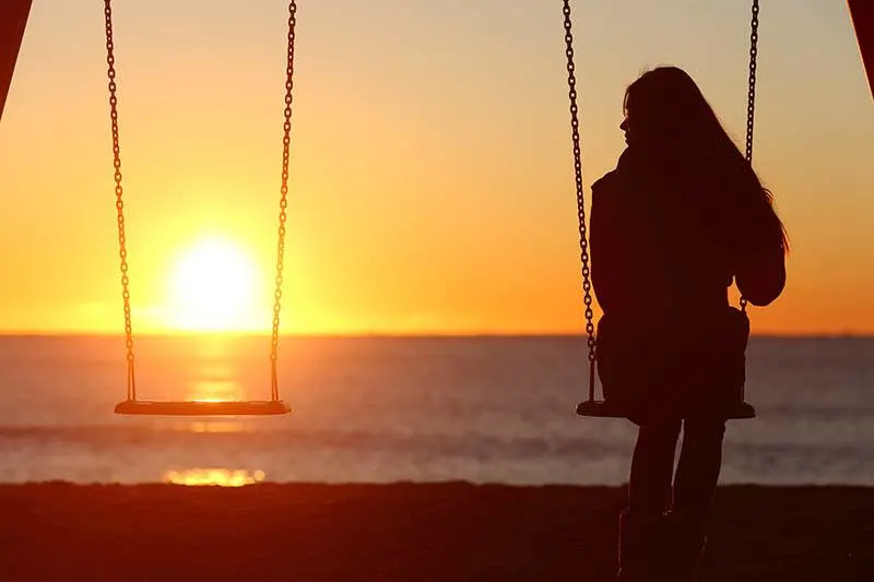 silhouette of woman sitting alone on swing in front of sea