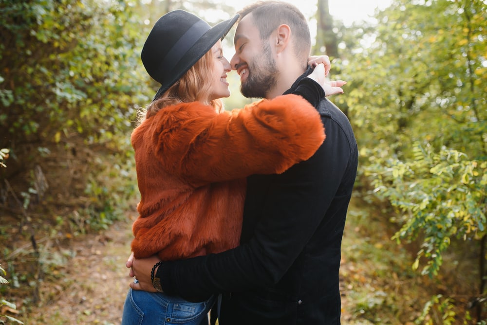 smiling attractive loving couple standing in the woods hugging