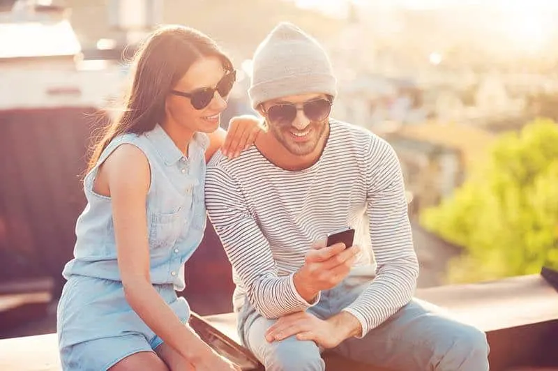 smiling man and woman looking at phone while sitting outside
