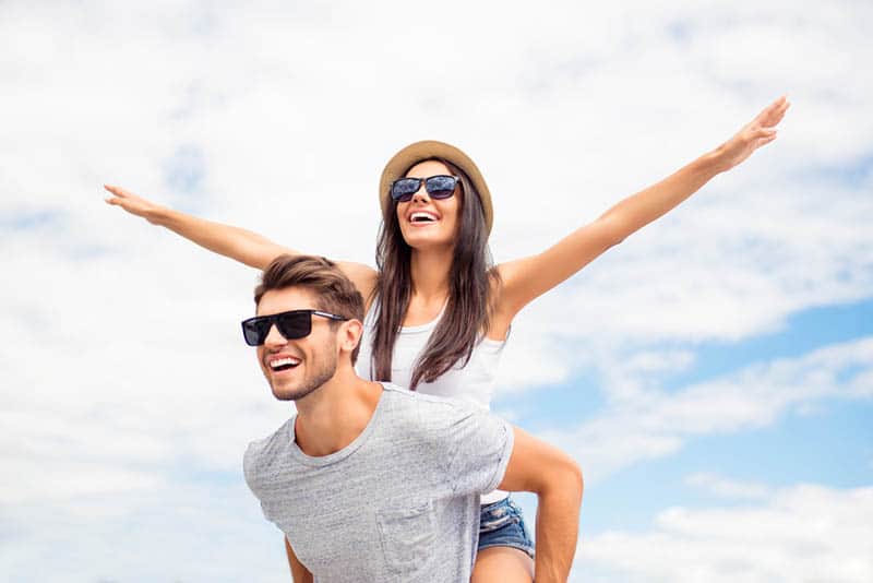 uomo sorridente che fa da cavalluccio a una donna all'aperto