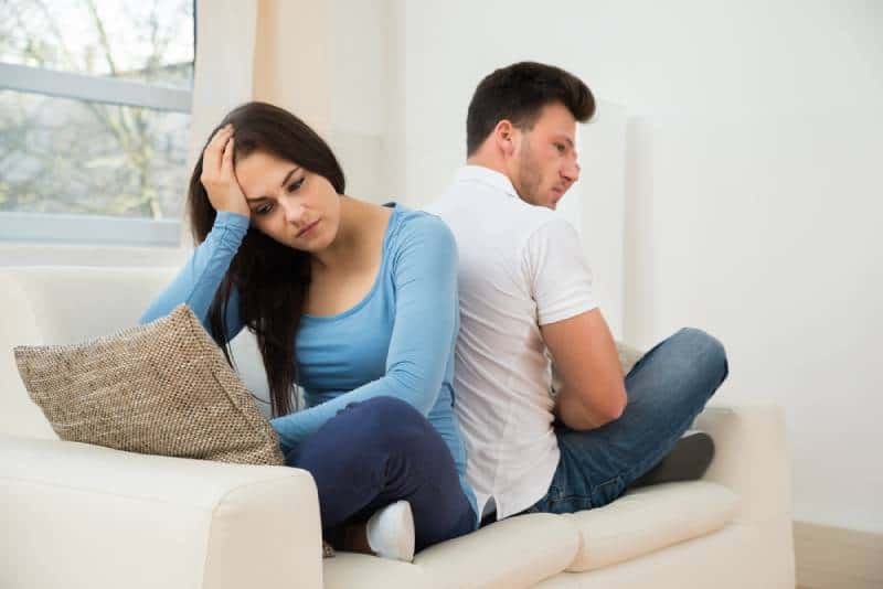 thoughtful couple sitting back to back on couch