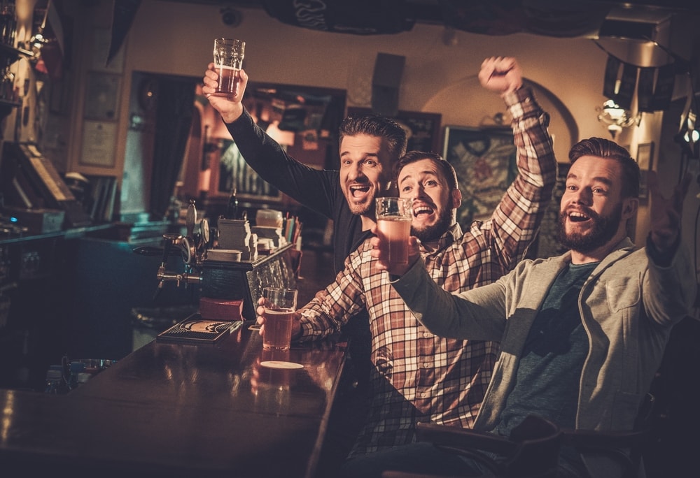 tre amici al bar che bevono birre e guardano una partita