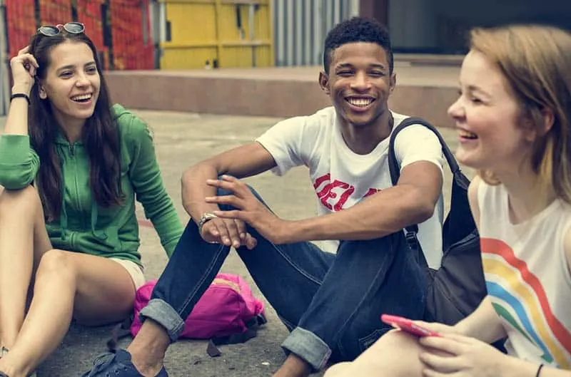 three smiling tenagers sitting outside