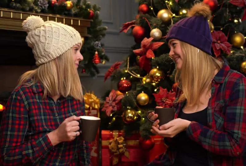 two girls sit under a christmas tree wearing hats