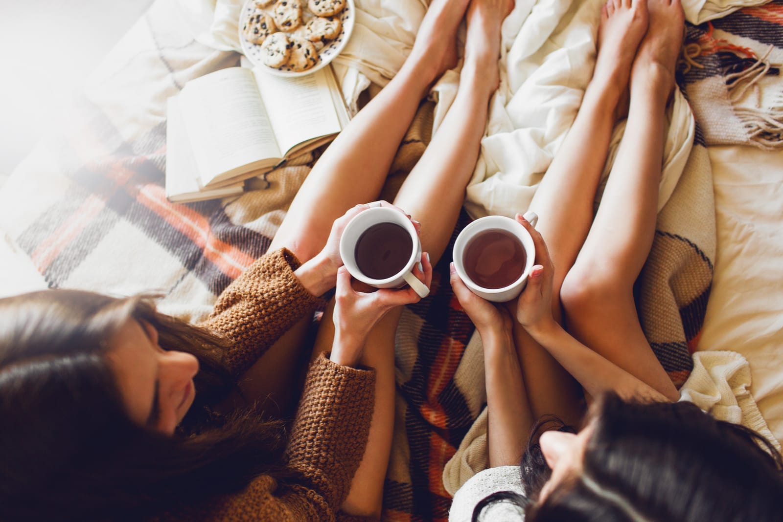 two sisters on the bed with old books and cup of tea in hands