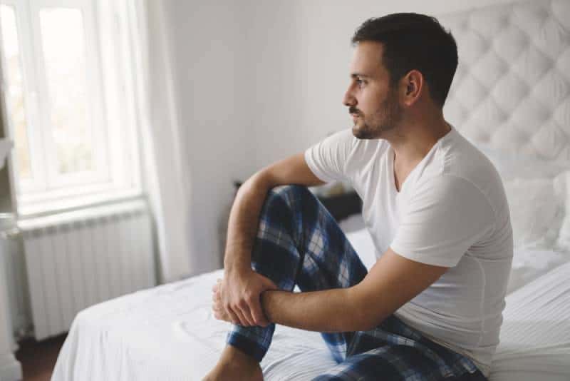 hombre infeliz en pijama sobre la cama