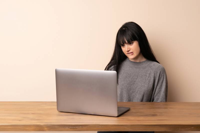 woman biting lips and looking at laptop