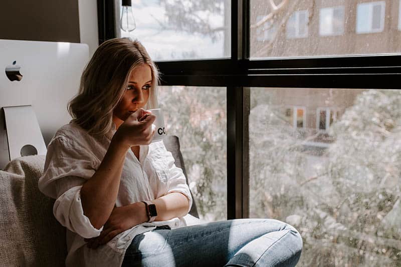 mujer bebiendo café junto a la ventana de su casa