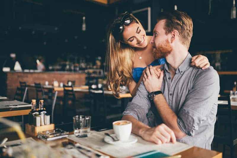 una mujer abraza a un hombre por detrás en una cafetería