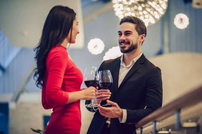 woman in red dress and handsome man in suit having conversation with glass of wine